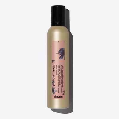 Frasco dourado com tampa preta e etiqueta rosa com flores azuis, mousse capilar Davines.