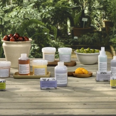 Produtos de cuidados pessoais variados em mesa de madeira com frutas e plantas ao fundo