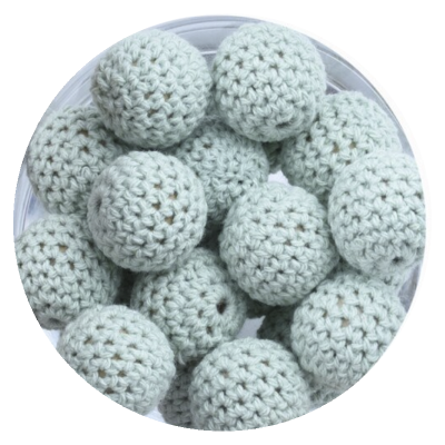 Bolas cinza claro em croché com textura trançada numa superfície branca circular