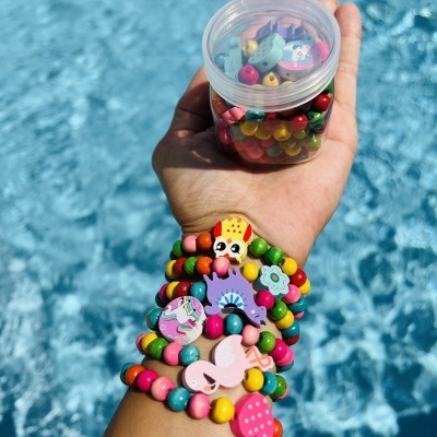 Braçadeiras coloridas com contas de madeira e enfeites divertidos, mão segurando frasco transparente com contas, fundo de água azul