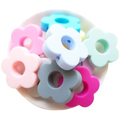 Contas flor coloridas de plástico com buracos centrais numa taça branca