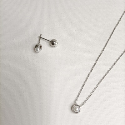 Brincos e colar de prata com pérolas sobre fundo branco.