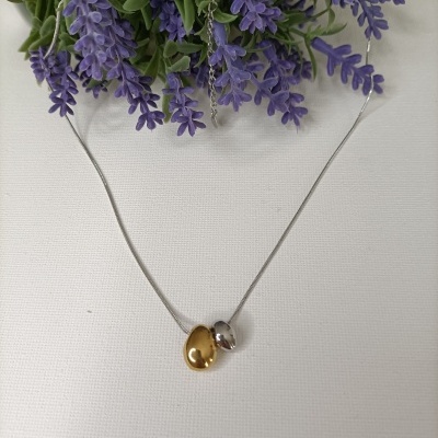 Colar com pendentes dourado e prateado sobre fundo branco e flores roxas