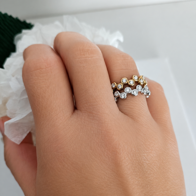 Mão com dois anéis, dourado e prateado, com pedras brilhantes e papel branco amassado.