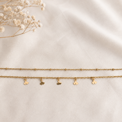 Duas pulseiras douradas finas sobre tecido branco com flores secas ao lado