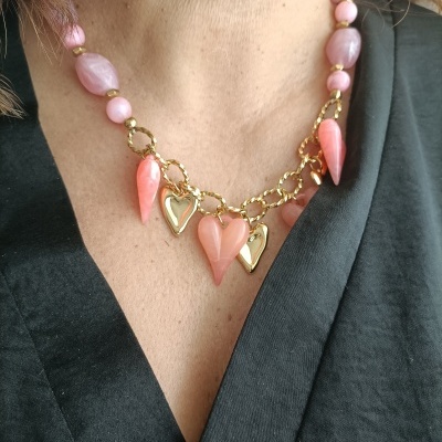 Colar com contas rosas e pendentes dourados em forma de coração, usado no pescoço sobre roupa preta.