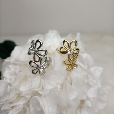 Dois anéis florais, um prateado e um dourado, sobre flor branca.