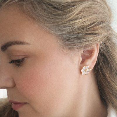 Brinco de flor dourado com esmalte branco no lóbulo da orelha de mulher com cabelo loiro.