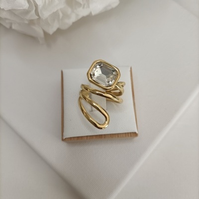 Anel dourado com pedra retangular transparente exposto em almofada branca