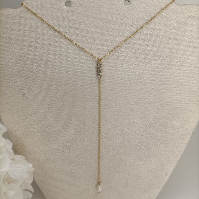 Colar dourado com pedras brilhantes e pérola, exposto em suporte bege