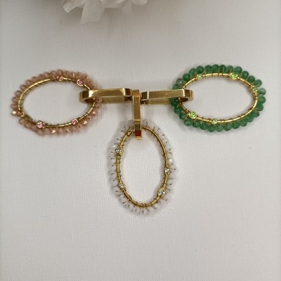 Pulseiras ovais com contas coloridas e fechos dourados sobre fundo branco