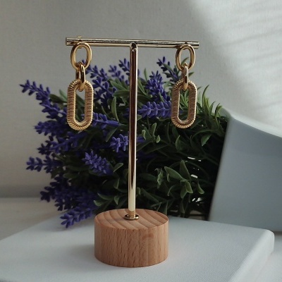 Brincos dourados pendurados em suporte metálico com base de madeira