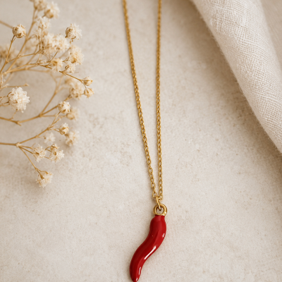 Colar dourado com pendente de pimenta vermelha em fundo claro com flores secas e tecido