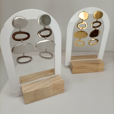 Brincos dourados e prateados em suportes brancos com base de madeira