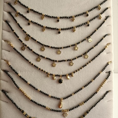 Pulseiras com contas pretas e detalhes dourados com vários pendentes, em fundo bege.