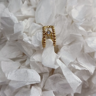 Anel dourado com bolas e pedra central sobre papel branco amassado