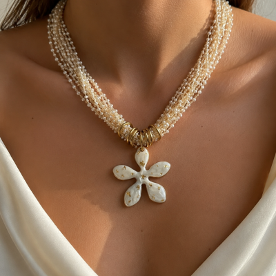 Colar de pérolas com pendente de flor creme e detalhes dourados no pescoço.