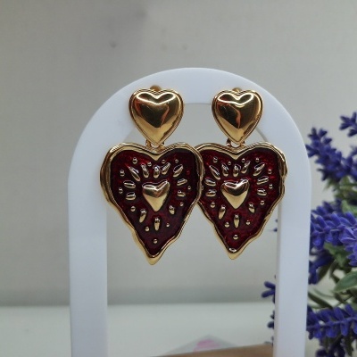 Brincos coração dourados com detalhe vermelho num suporte branco