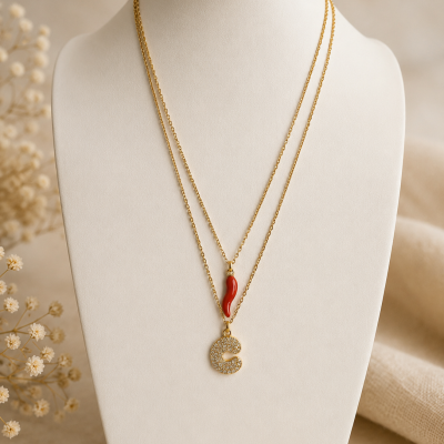 Colar duplo dourado com pendente de chifre vermelho e letra C brilhante num busto branco