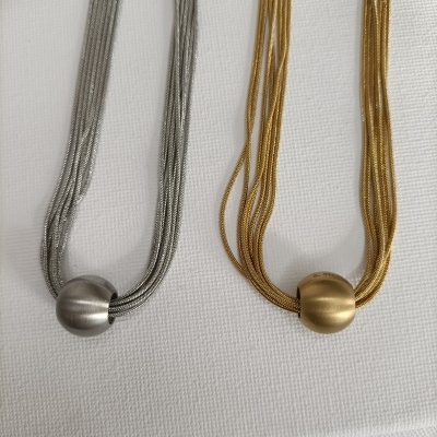 Colares prateado e dourado com elemento redondo metálico no centro em fundo branco.