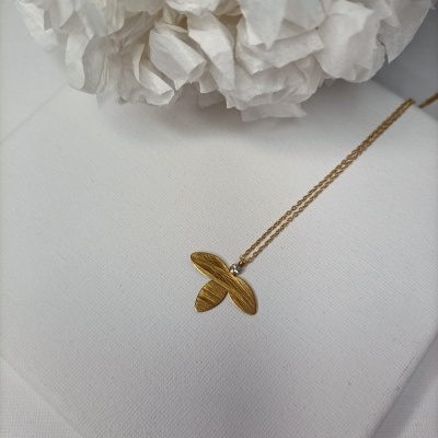 Colar dourado com pendente em forma de pétalas e pedra brilhante sobre superfície branca com flor branca