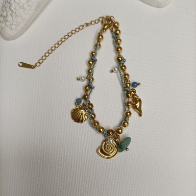 Pulseira dourada com pendentes e pedras azuis sobre fundo branco