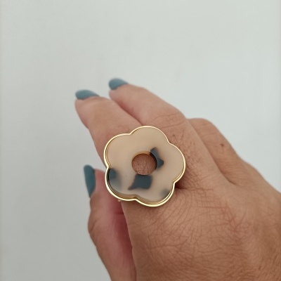 Anel flor bege com manchas pretas e contorno dourado numa mão com unhas azul esverdeado