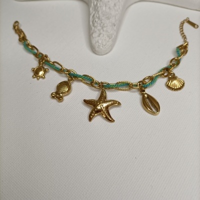 Pulseira dourada com pendentes marítimos e fio azul entrelaçado.