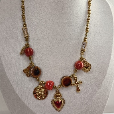 Colar dourado com contas vermelhas e castanhas e pingentes diversos sobre busto cinza