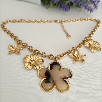 Colar dourado com pendentes em forma de flores douradas e resinadas com padrão marmoreado bege e castanho.