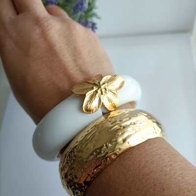 Braçadeiras branca com flor dourada e dourada martelada num pulso