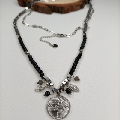 Colar com pendentes prateados e contas pretas sobre fundo branco e base de madeira