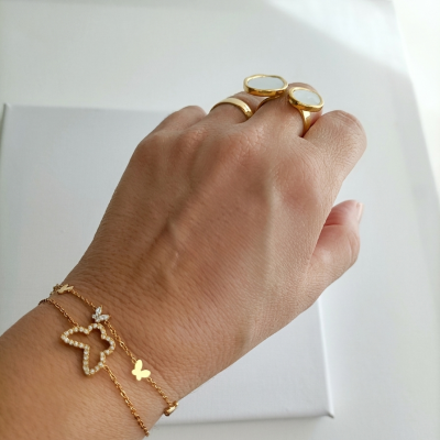 Mão com duas argolas douradas com pedras brancas e pulseira dourada com pingentes de borboleta