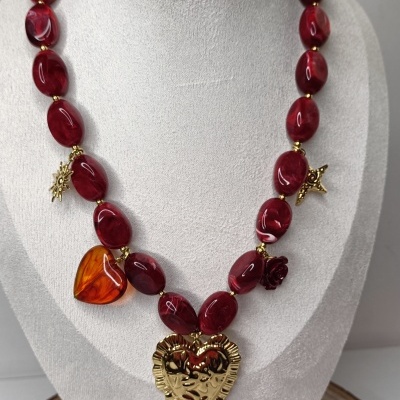 Colar com contas vermelhas e pingentes dourados em suporte branco.
