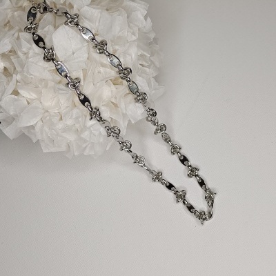 Colar prateado com elos ovais entrelaçados sobre fundo branco com flores de papel