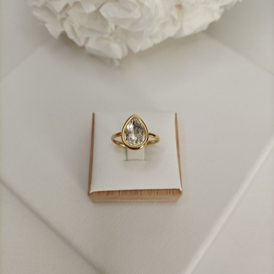 Anel dourado com pedra transparente em forma de gota num suporte branco