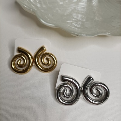 Brincos dourados e prateados em forma de espiral sobre fundo branco e prato decorativo branco