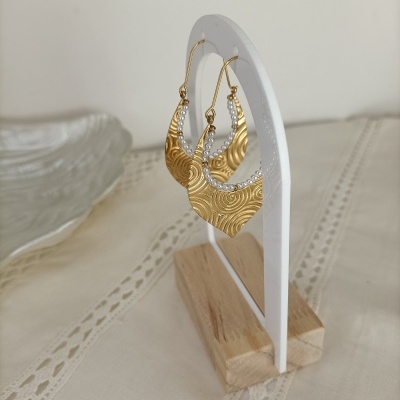 Brincos dourados texturizados com pérolas em suporte branco com base de madeira.