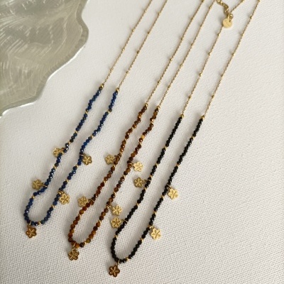 Três colares dourados com pedrinhas coloridas e pendentes de flor sobre fundo branco