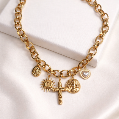 Colar dourado com pendentes variados sobre pano branco