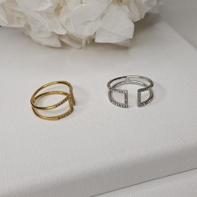 Dois anéis abertos, dourado e prateado, com pedras brilhantes sobre superfície branca