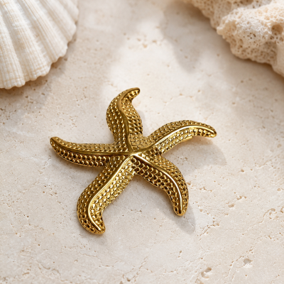 Estatueta dourada estrela-do-mar com textura pontilhada sobre superfície clara com conchas e coral