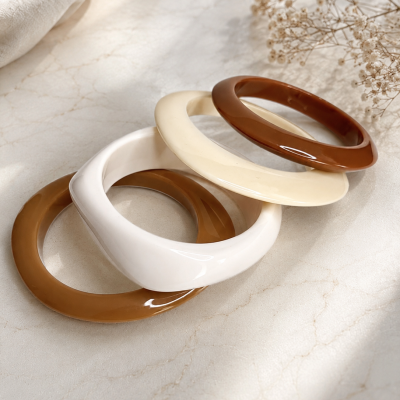 Pulseiras de plástico em tons castanho, bege e branco sobre fundo marmoreado.