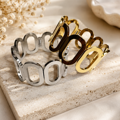 Duas pulseiras metálicas dourada e prateada com elos ovais sobre placa de pedra clara.