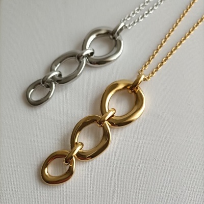 Dois colares com elos grandes, um prata e um dourado, sobre fundo branco.