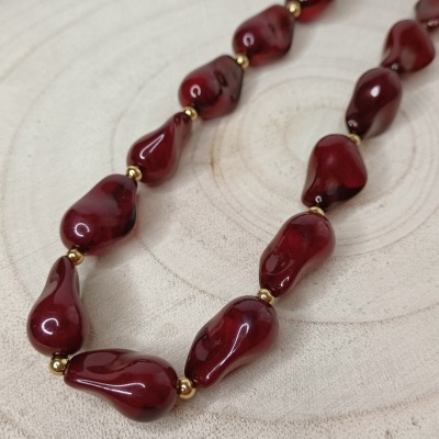 Colar com contas vermelhas e douradas sobre madeira