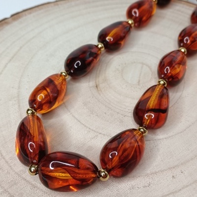 Colar de contas âmbar laranja com esferas douradas sobre madeira