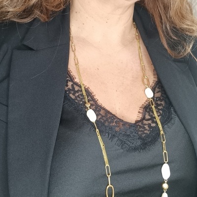 Colar dourado com contas brancas e brinco pendente branco, vestido com camiseta preta de renda e blazer preto