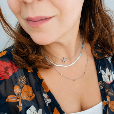 Colar feminino prateado com pingente de estrela usado em mulher com blusa floral