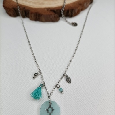 Colar prateado com pendentes azul e metálicos sobre tecido branco e base de madeira